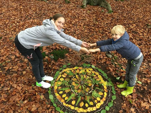 Mutter und Sohn halten einander über einem Kunstwerk aus Blättern und Zweigen an den Händen.
