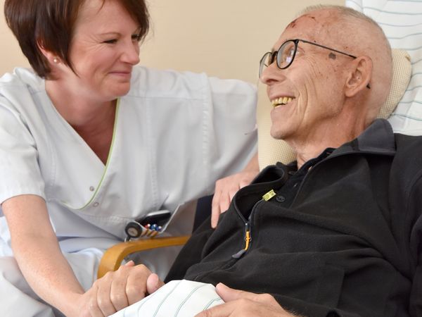 Pflegerin und sterbenskranker Patient lächeln sich an.